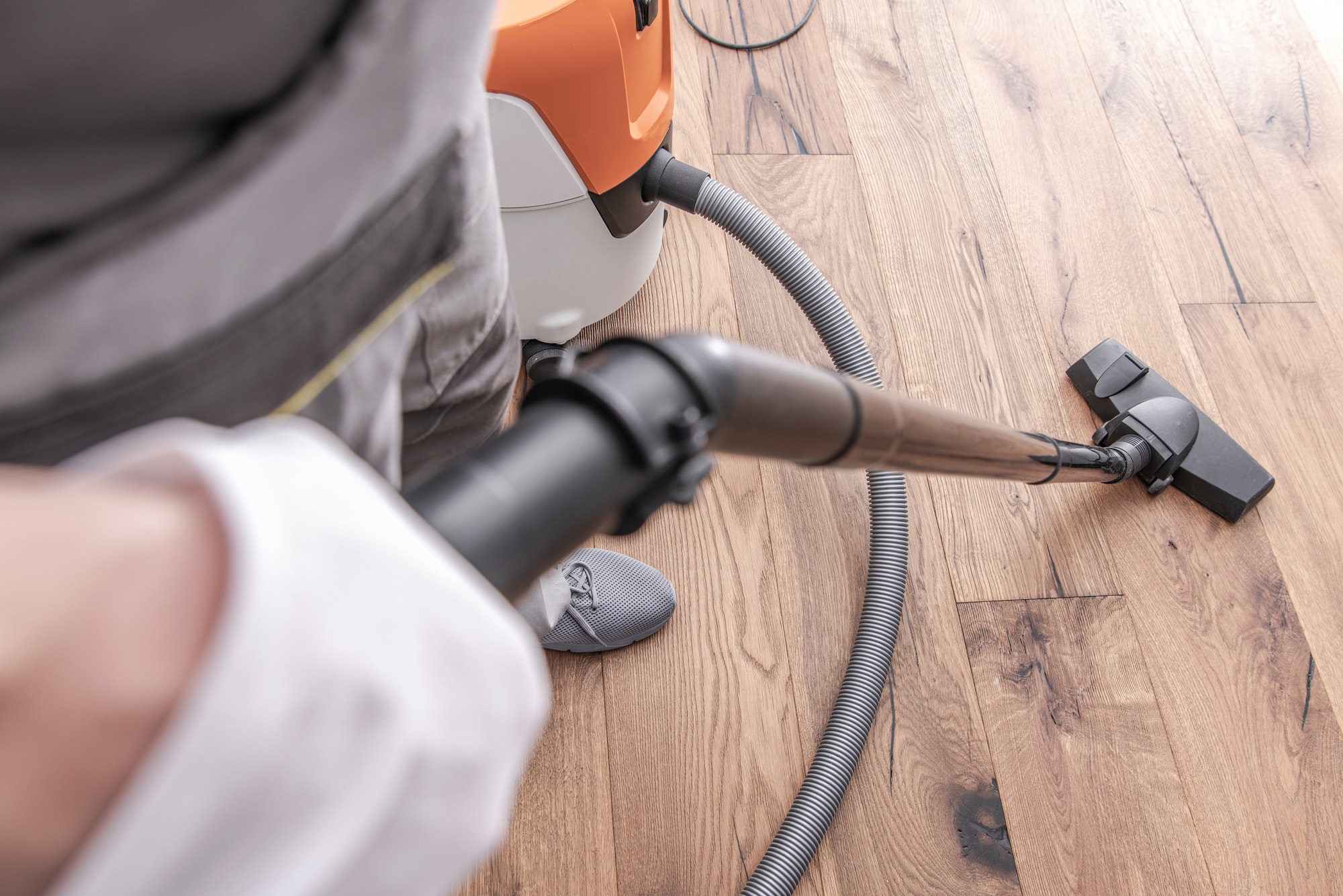 Worker vacuuming newly installed hardwood flooring with a professional cleaning machine.