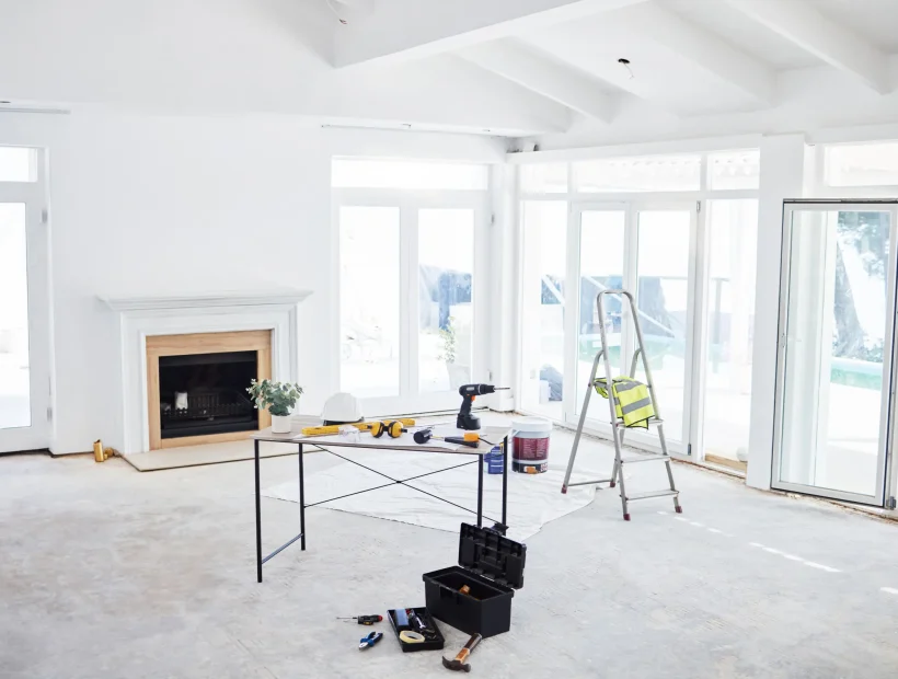 Bright living room undergoing whole-home renovation with tools, ladder, fireplace, and new windows