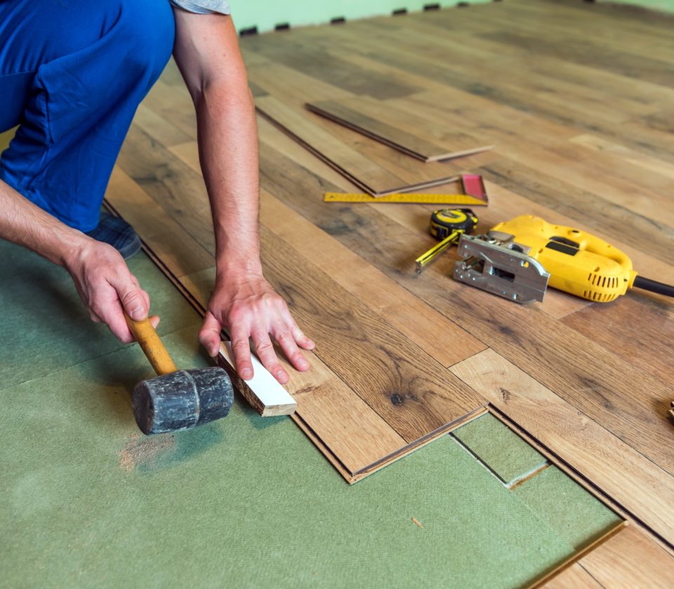 Installer fitting laminate flooring with a mallet and tools over underlayment.
